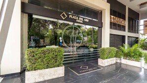 The entrance of Plaza Del Lili Hotel with a modern design, featuring a glass facade, a logo above the entrance, and potted plants in front. - Hotel Plaza Del Lili (Cali)