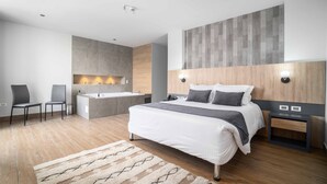 A modern bedroom with a large bed, a built-in bathtub, and a seating area with chairs. - Hotel Plaza Del Lili (Cali)