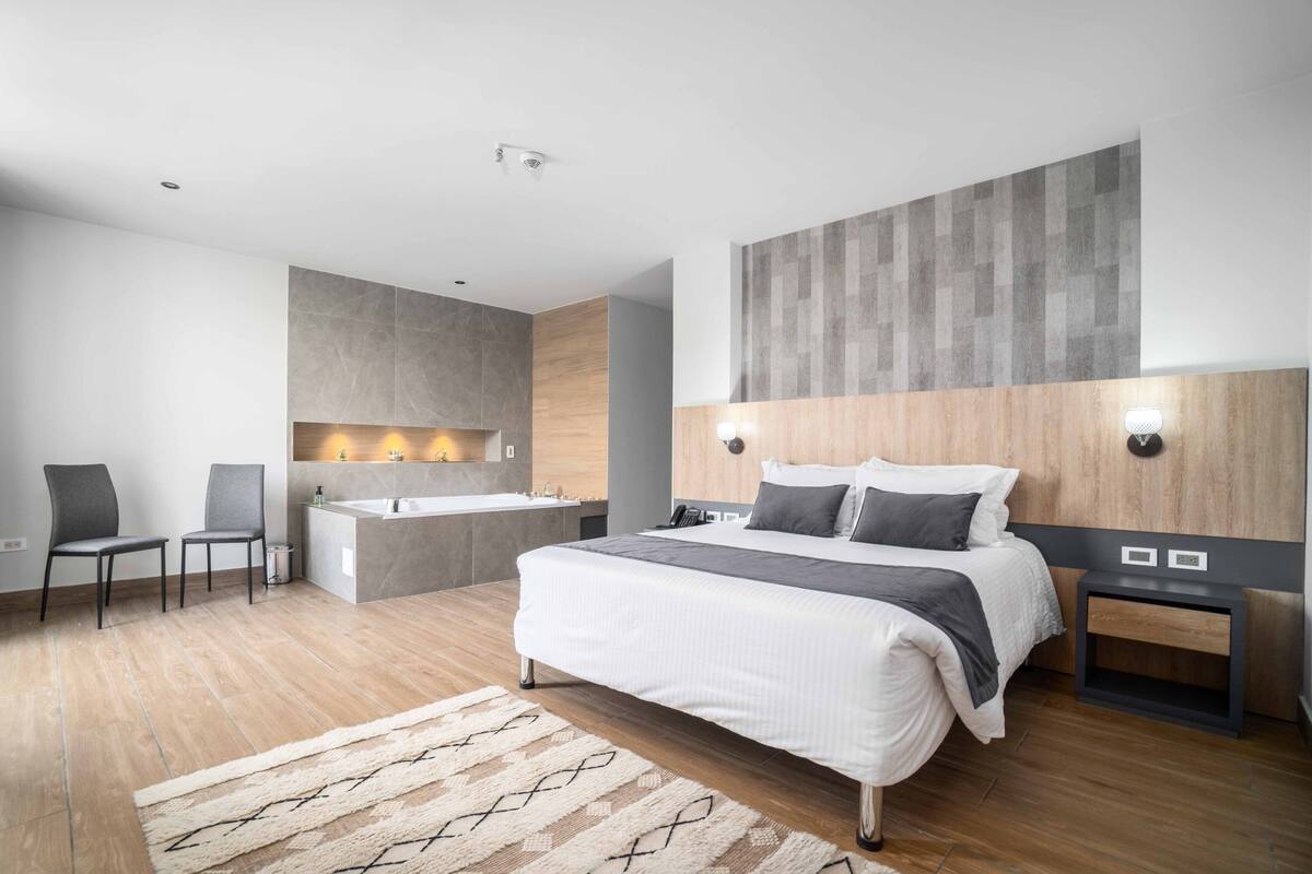A modern bedroom with a large bed, a built-in bathtub, and a seating area with chairs.