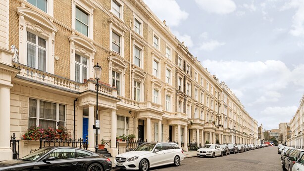 Une rangée de maisons de ville traditionnelles en briques, toutes dotées d’une architecture uniforme, sous un ciel dégagé, avec des voitures garées le long de la rue.