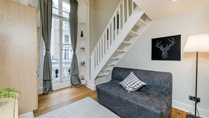 Un salon moderne avec un canapé gris, un escalier et une œuvre d’art représentant une tête de cerf noire accrochée au mur.
