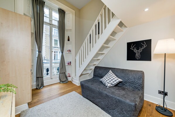 A modern living room with a grey sofa, a staircase, and a black deer head artwork on the wall.