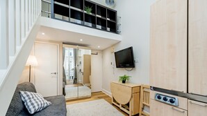 Un appartement moderne avec une chambre en mezzanine, un bureau en bois, une télévision et un coin cuisine.