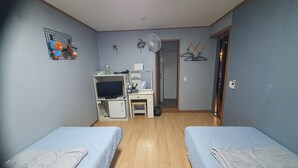 Una habitación con dos camas, un escritorio con computadora, televisión y un refrigerador pequeño.