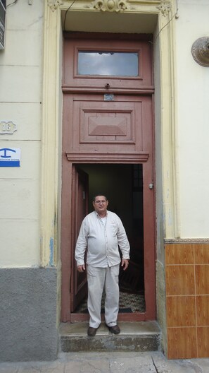 A man standing in a doorway with a brown door and a small window above it. - Hostal Vista Al Puerto (Havana)