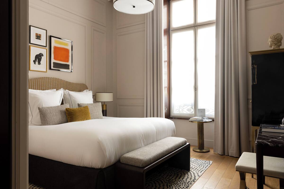Een hotelkamer met een groot bed, een nachtkastje, een bureau en een raam met gordijnen.