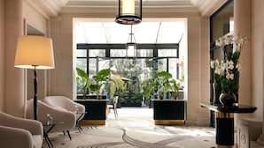 Een ruime lobby met een moderne kroonluchter, comfortabele zitmogelijkheden, plantenbakken en een groot raam met uitzicht op groen.