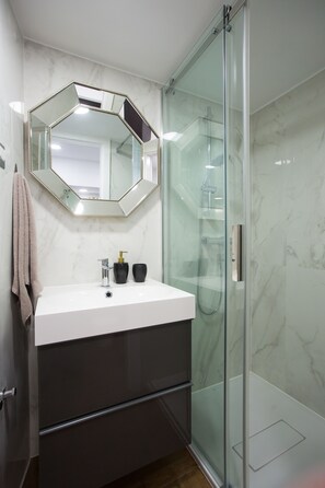 A modern bathroom with a white sink, a large mirror, and a glass-enclosed shower.