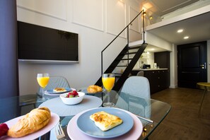A breakfast setting with croissants, a bowl of fruit, and orange juice on a glass table. - Apartments Zagreb1875 (Zagreb)