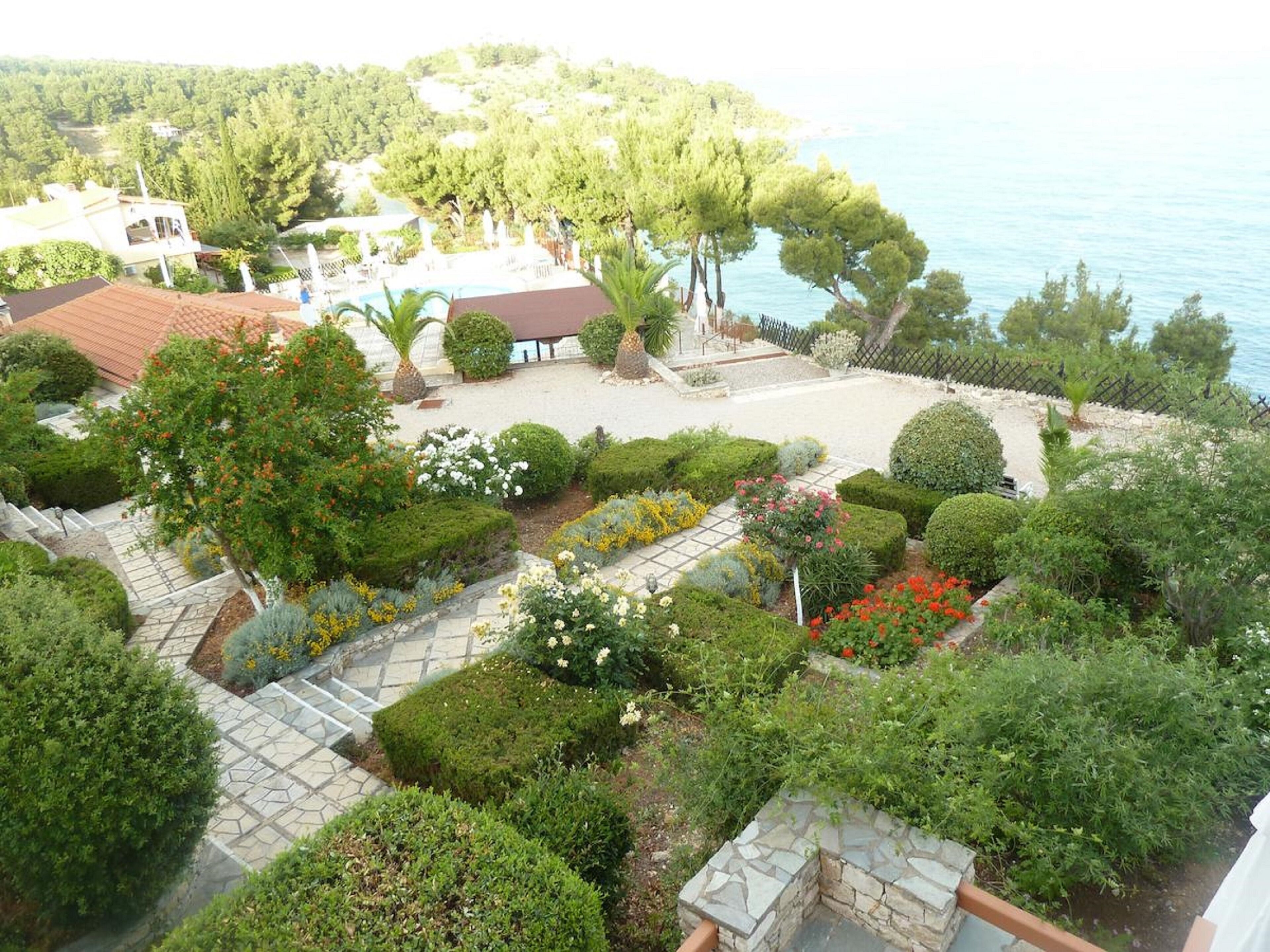 Un jardín ajardinado con un sendero de piedra, diferentes arbustos y vistas al mar.