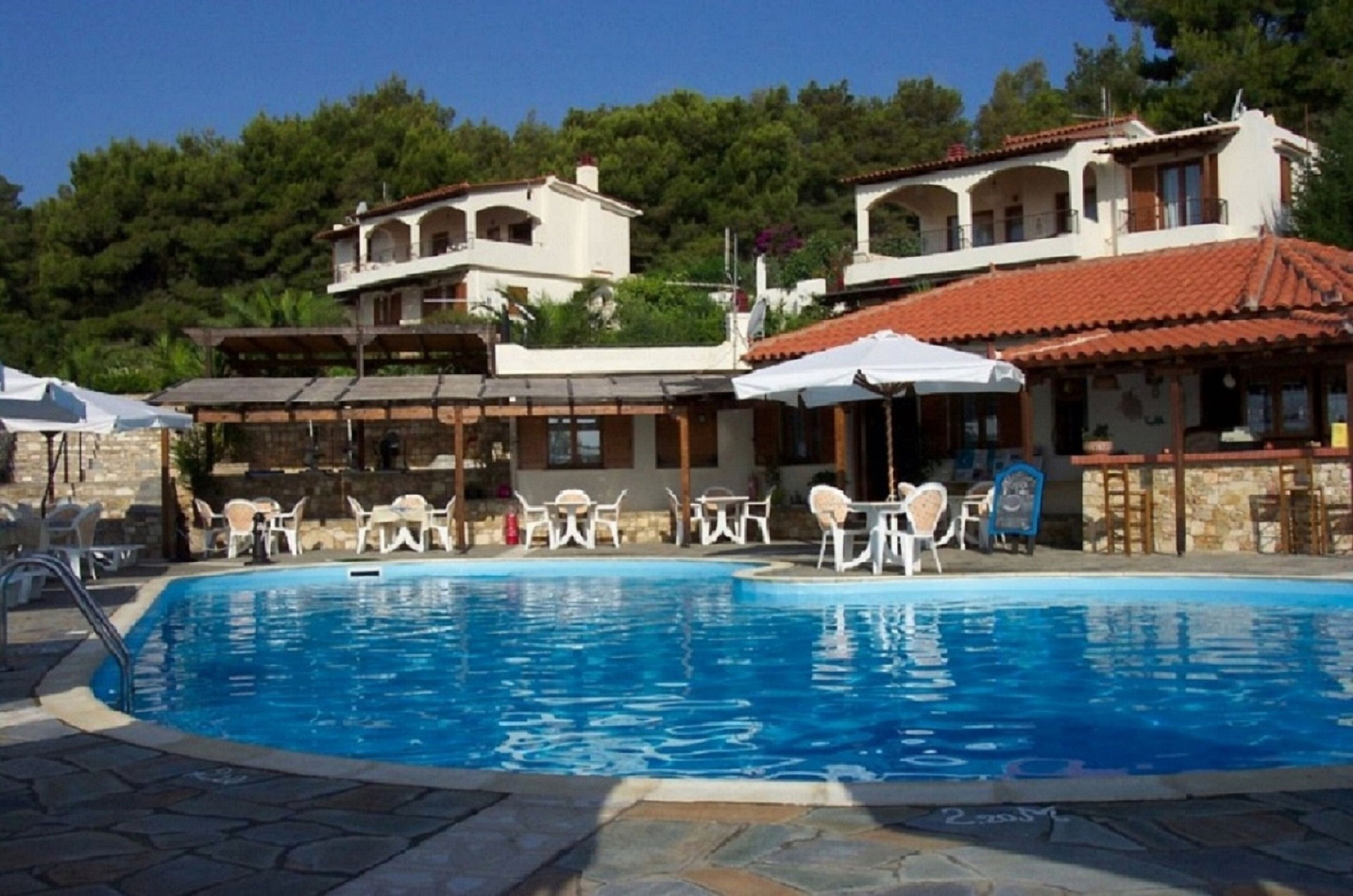 A swimming pool with lounge chairs and umbrellas, surrounded by buildings with a Mediterranean architectural style.