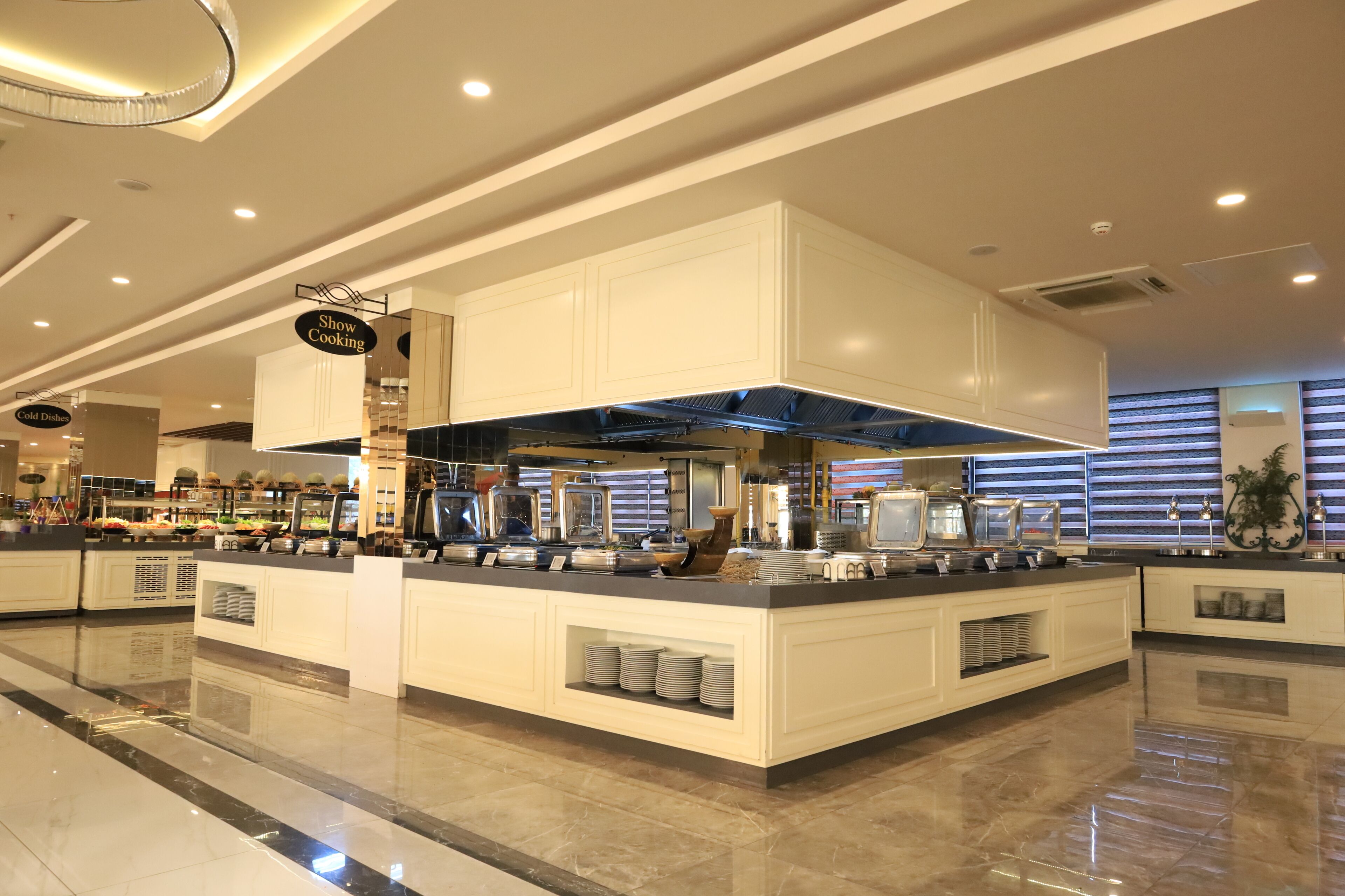 A modern buffet setup with a central island, overhead ventilation, and a 'Show Cooking' sign.