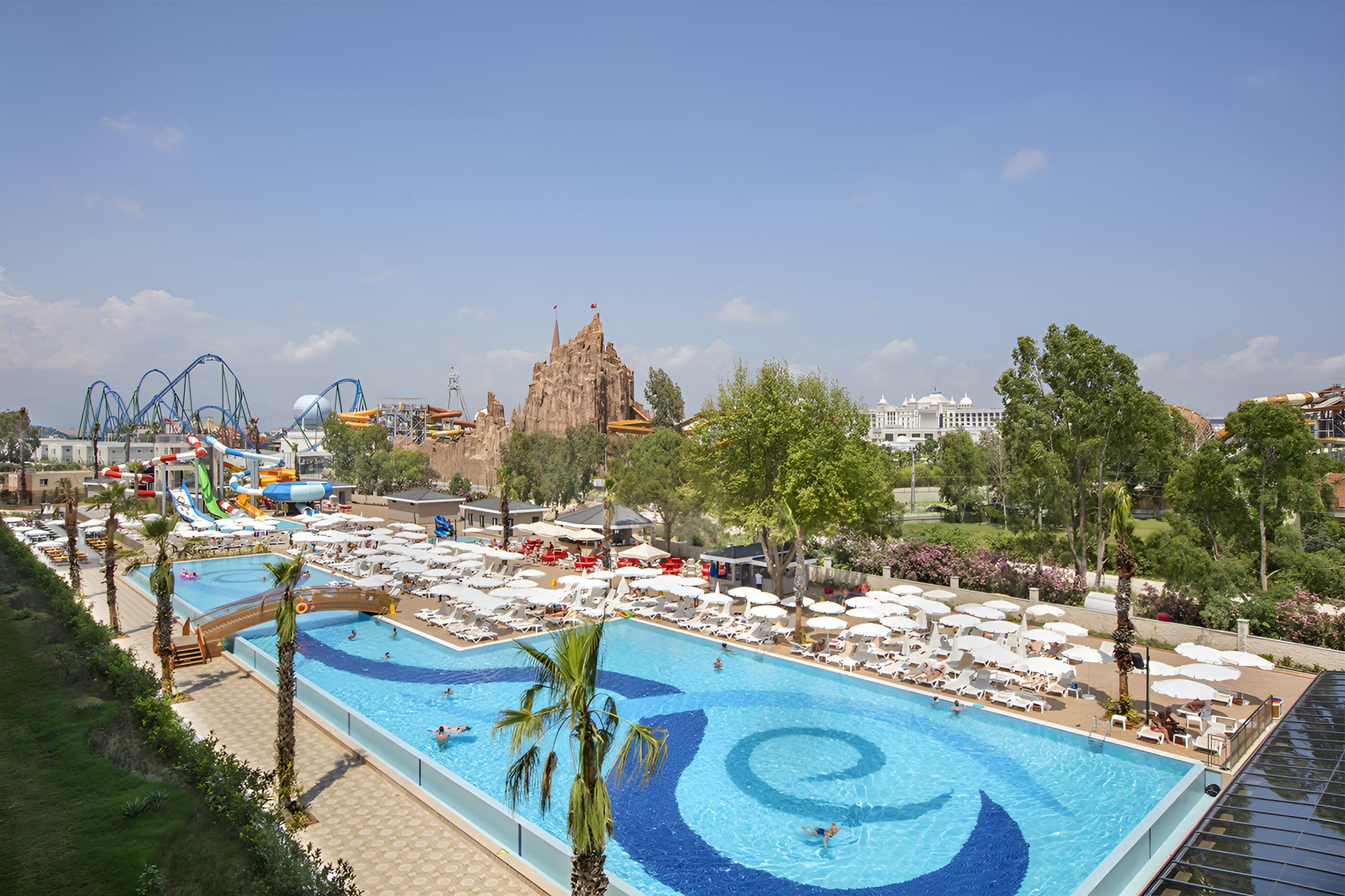 A large swimming pool with a water slide, surrounded by sun loungers and umbrellas.