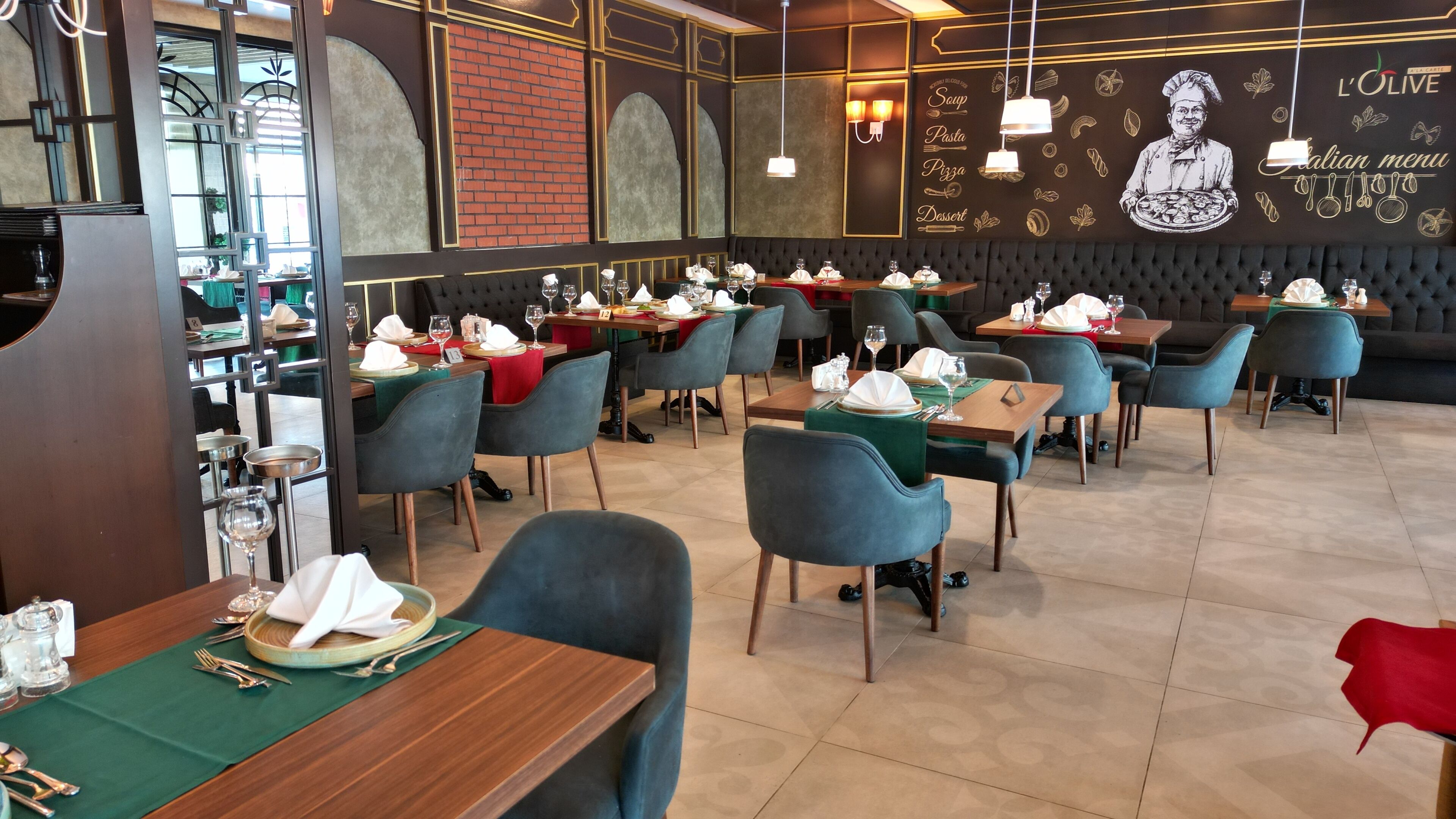 Interior de un restaurante con varias mesas y sillas, una pared de ladrillo y un mural en la pared de fondo.