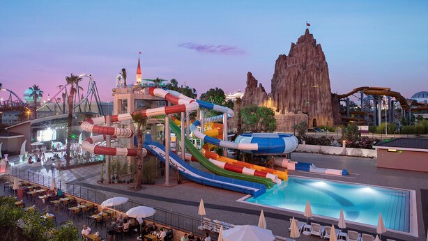 Un parque acuático con una piscina grande, toboganes y una estructura que parece una montaña al fondo.