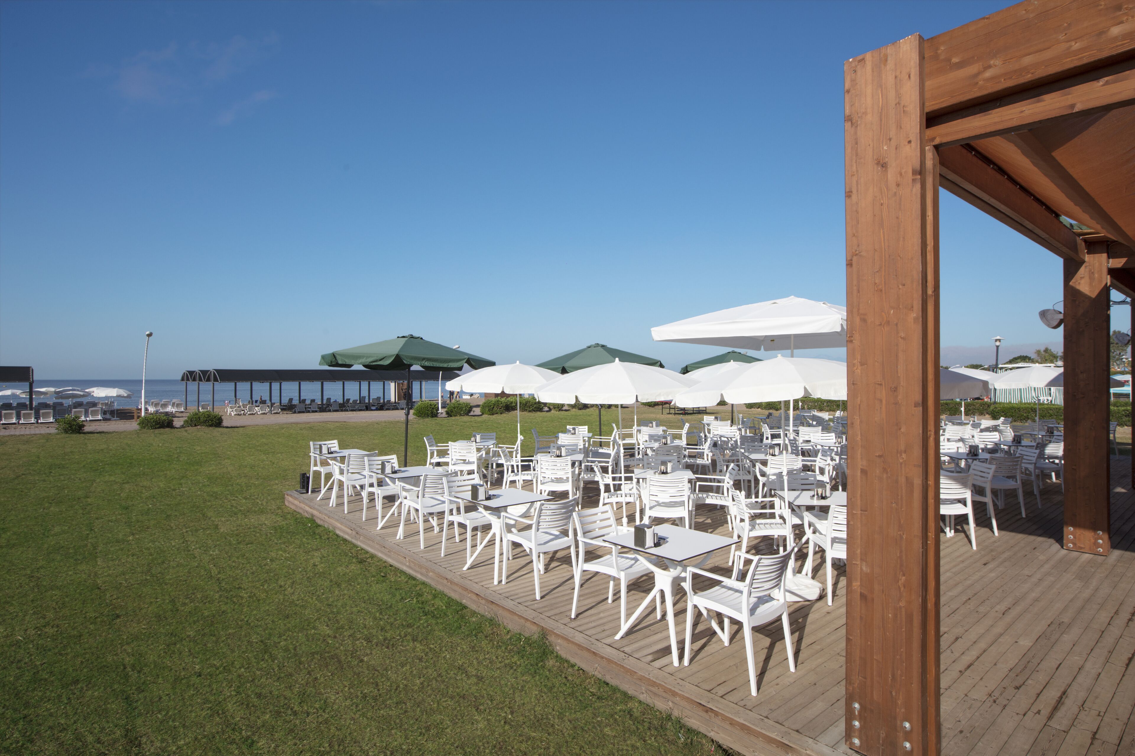 Un área de comedor al aire libre con sillas y mesas blancas, rodeada de sombrillas y vistas a un cuerpo de agua.
