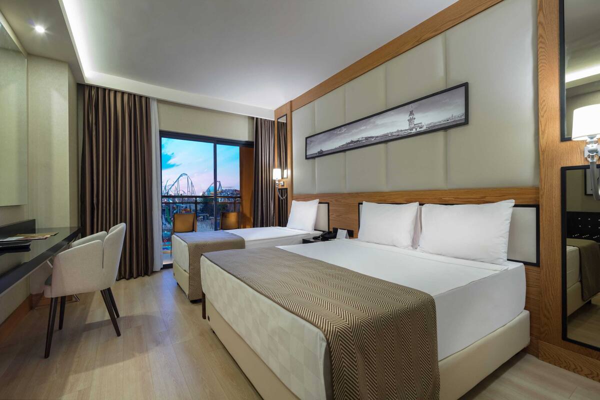 A hotel room with a bed, a desk, a chair, a television, and a view of a cityscape.