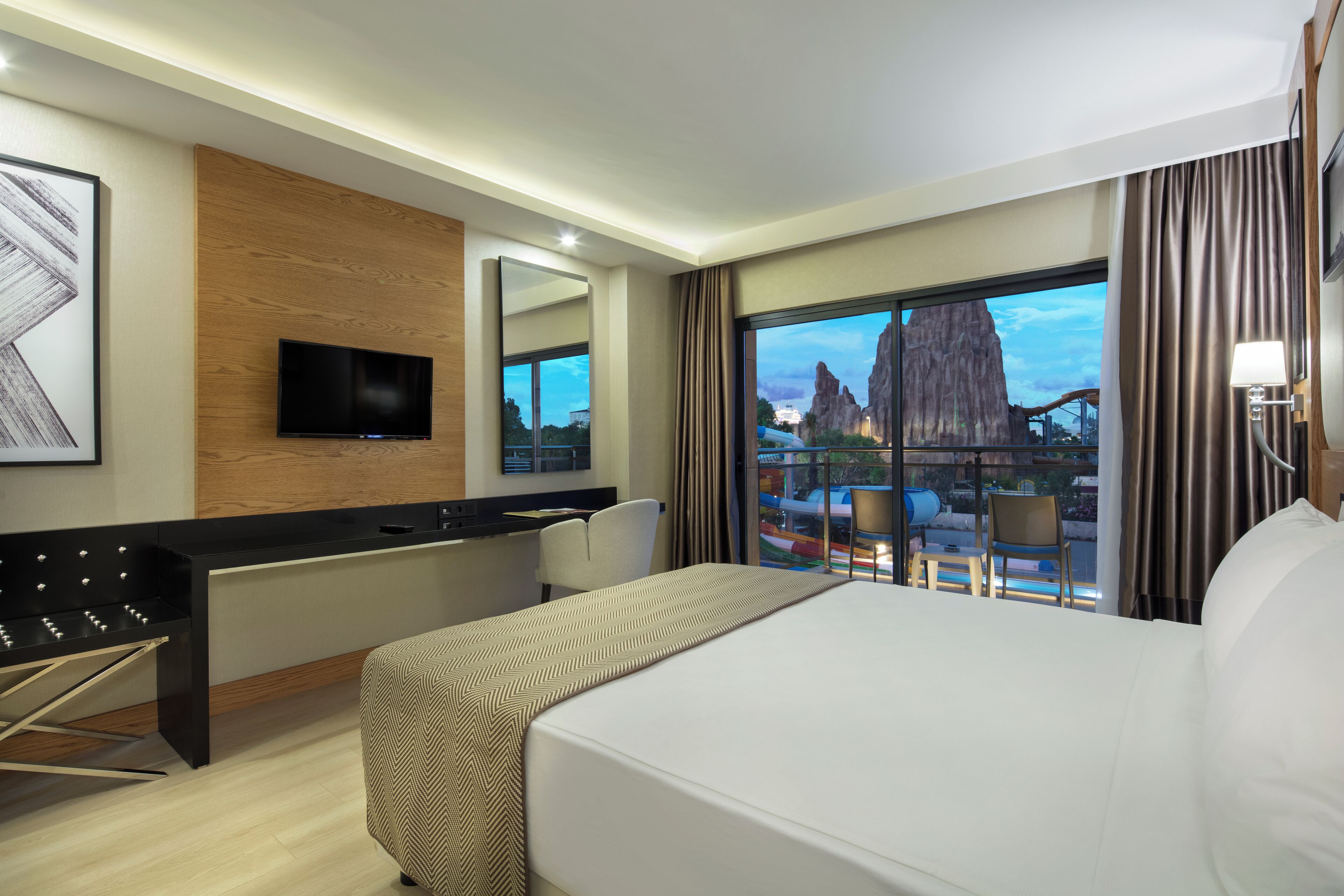 Ein Hotelzimmer mit Bett, Schreibtisch, Stuhl, Fernseher und einem großen Fenster mit Blick auf eine Felsformation und eine Brücke.