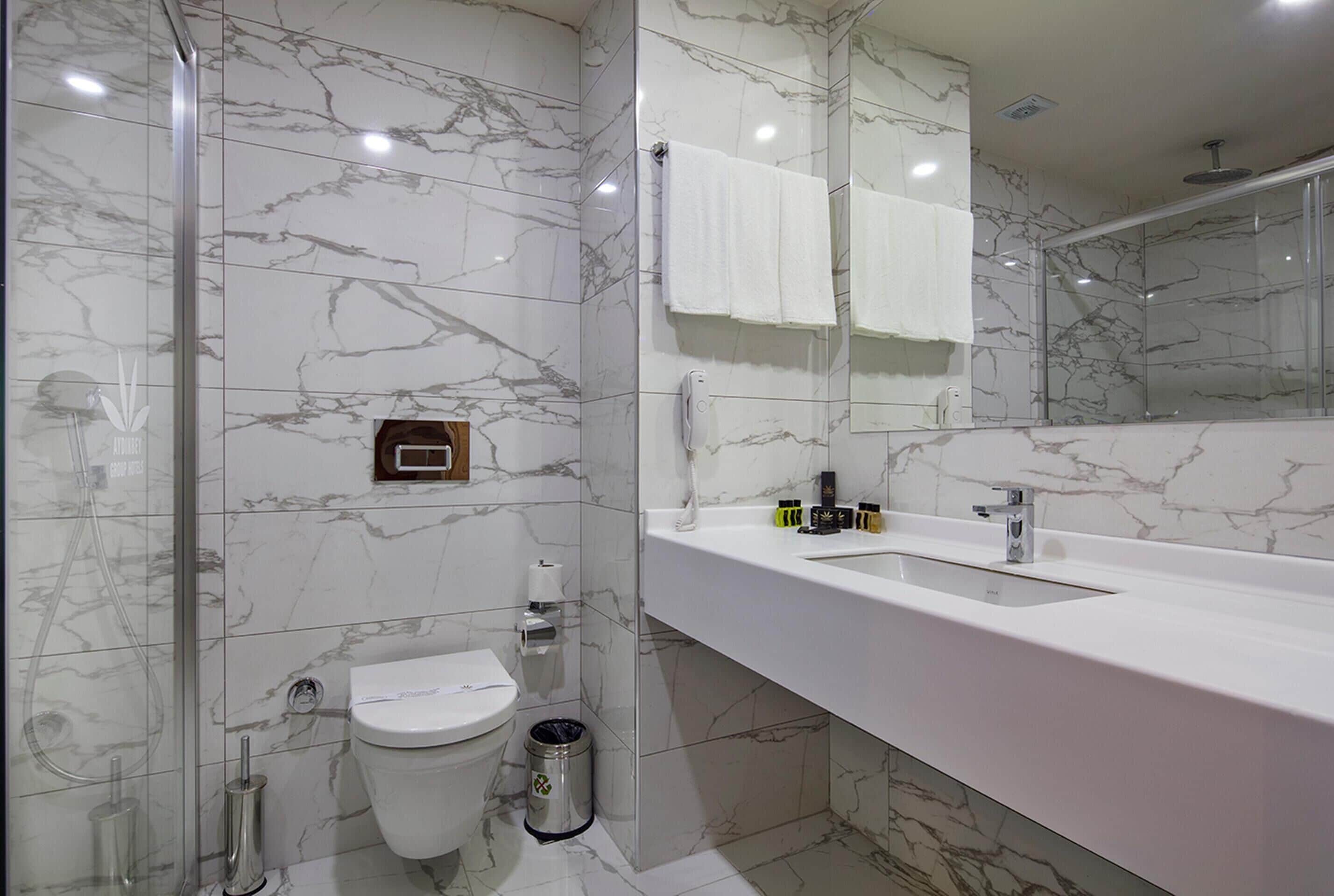 A modern bathroom with a marble backsplash, a glass shower enclosure, a white sink, and a toilet.