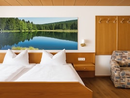 Quarto com uma cama grande, uma mesa de cabeceira, um guarda-roupa de madeira, uma poltrona estampada e um quadro na parede de um lago.