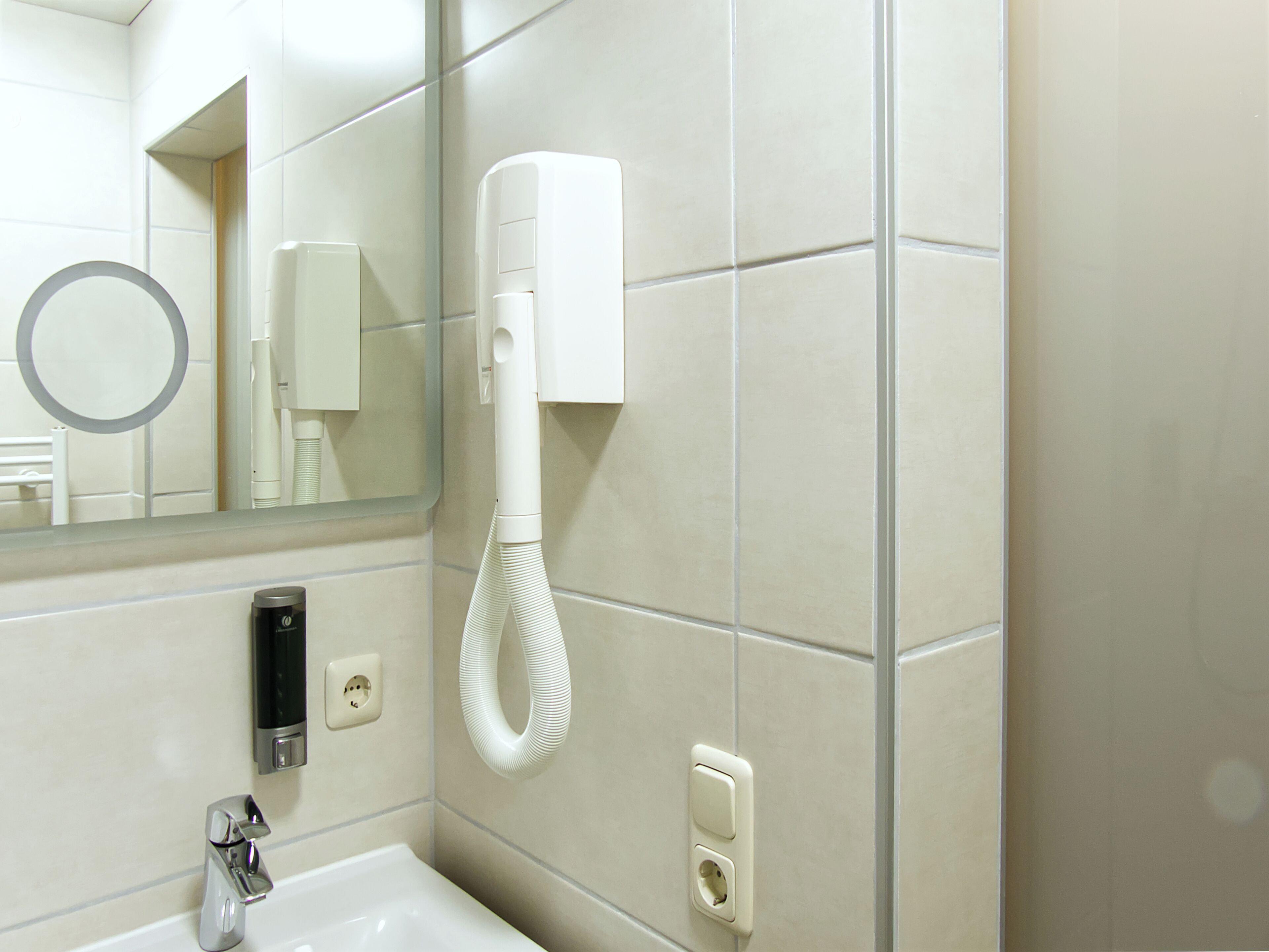 Une salle de bain équipée d’un lavabo, d’un miroir, d’un sèche-cheveux et d’un distributeur de serviettes.