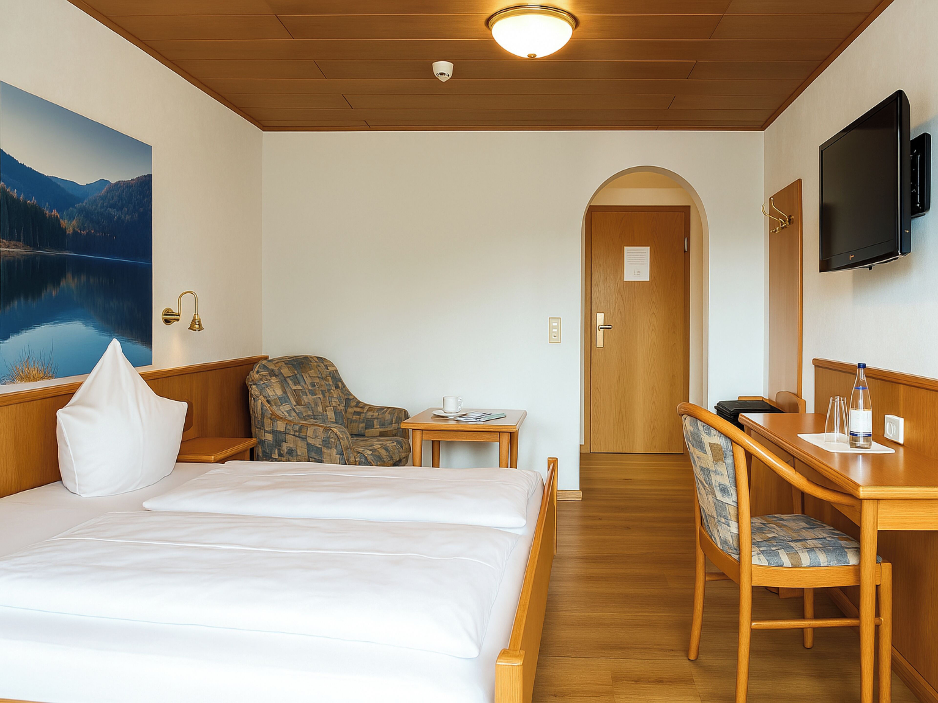 Een hotelkamer met een bed, een bureau, een stoel, een televisie en een schilderij van een meer.