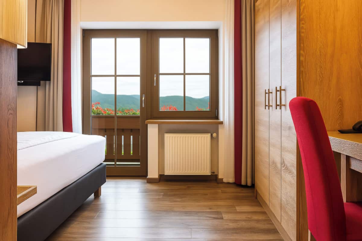 Une chambre d’hôtel comprenant un lit, un bureau, une chaise, une télévision, une fenêtre donnant sur les montagnes et un radiateur.
