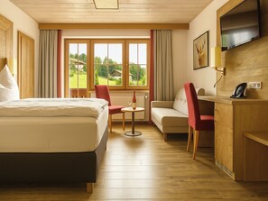 A hotel room with a bed, a small round table, a sofa, and a TV mounted on the wall. - Hotel zur Linde (Lohberg)
