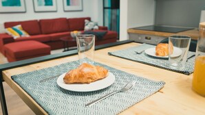 A breakfast setup with croissants on a patterned placemat, a glass of water, and a glass of orange juice on a wooden table. - Apartments Franky6 (Zagreb)