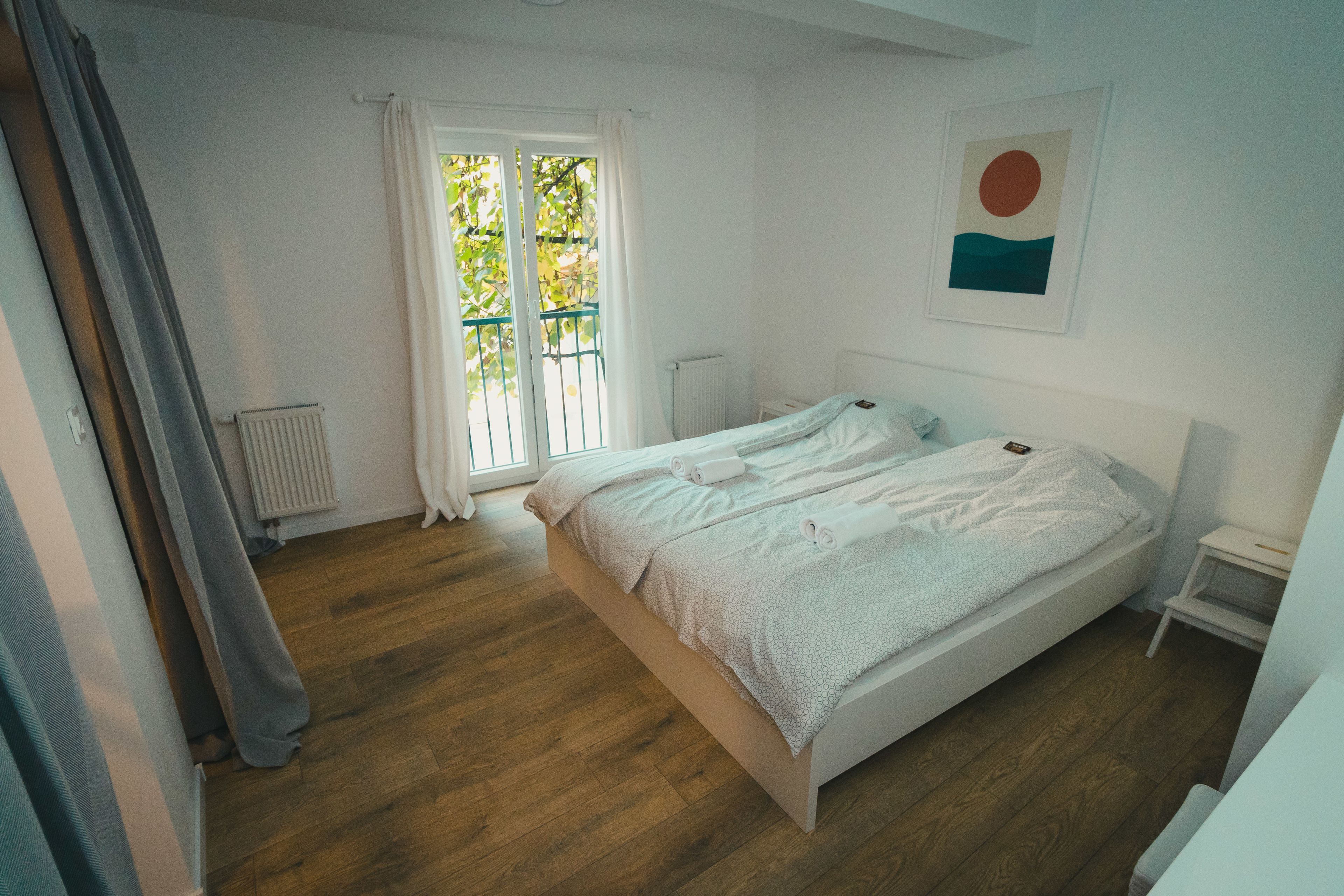 A bedroom with a bed, a radiator, a window with curtains, and a small bedside table.
