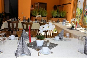 Un restaurante con mesas dispuestas para comer, con manteles blancos, servilletas ordenadas y plantas en macetas.