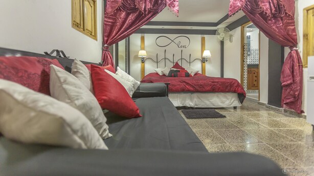 Een slaapkamer met twee bedden, rood-wit beddengoed, een zwarte bank en een plafondventilator.
