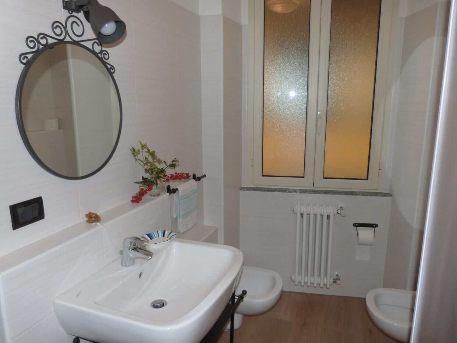 Ein Badezimmer mit Waschbecken, runder Spiegel, Toilette und Fenster mit Milchglas.