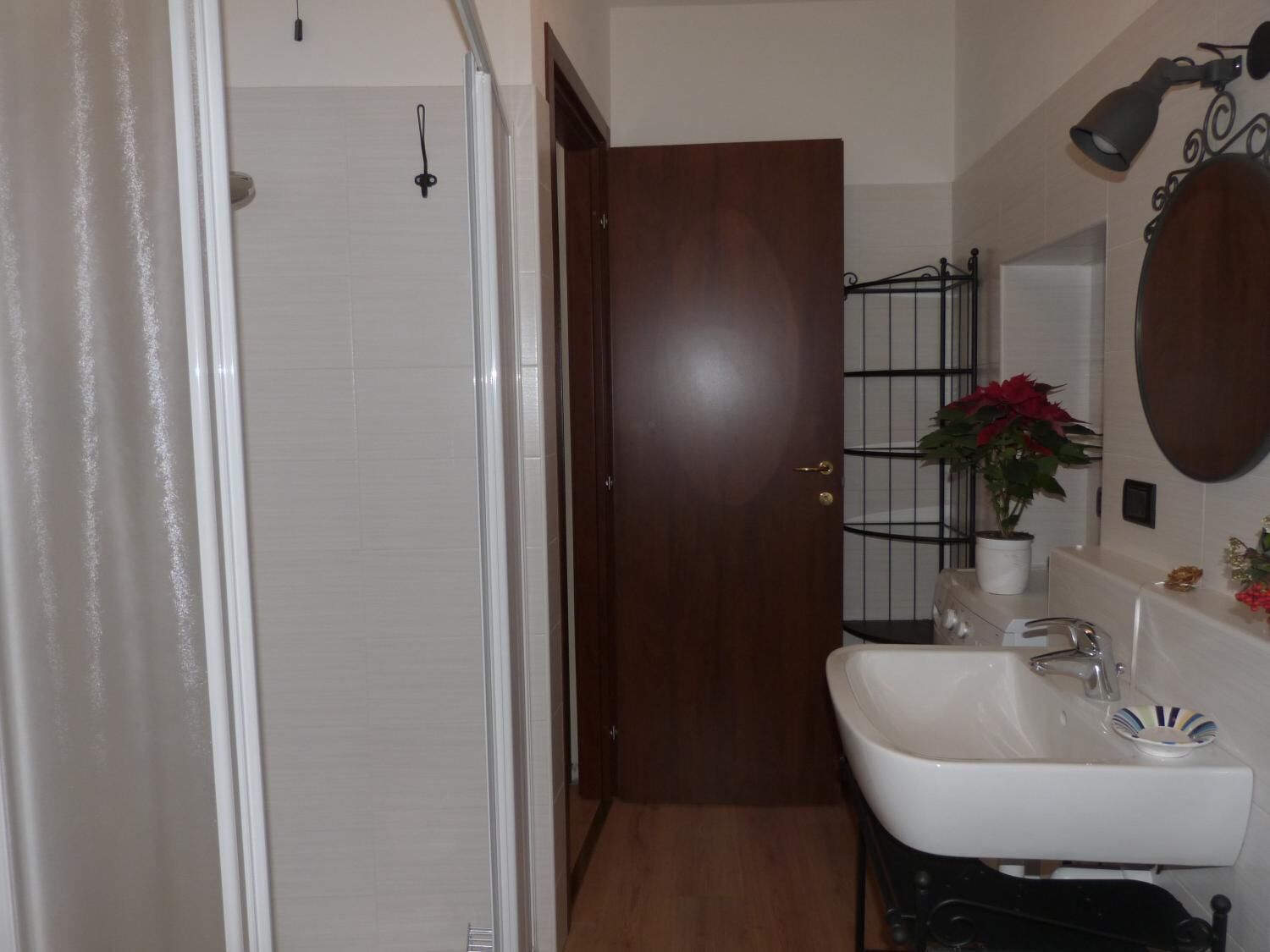 Un bagno con lavandino bianco, uno specchio, una doccia e una porta in legno.