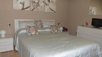 Un dormitorio con cama, mesitas de noche, cómoda, televisor y decoración en la pared.