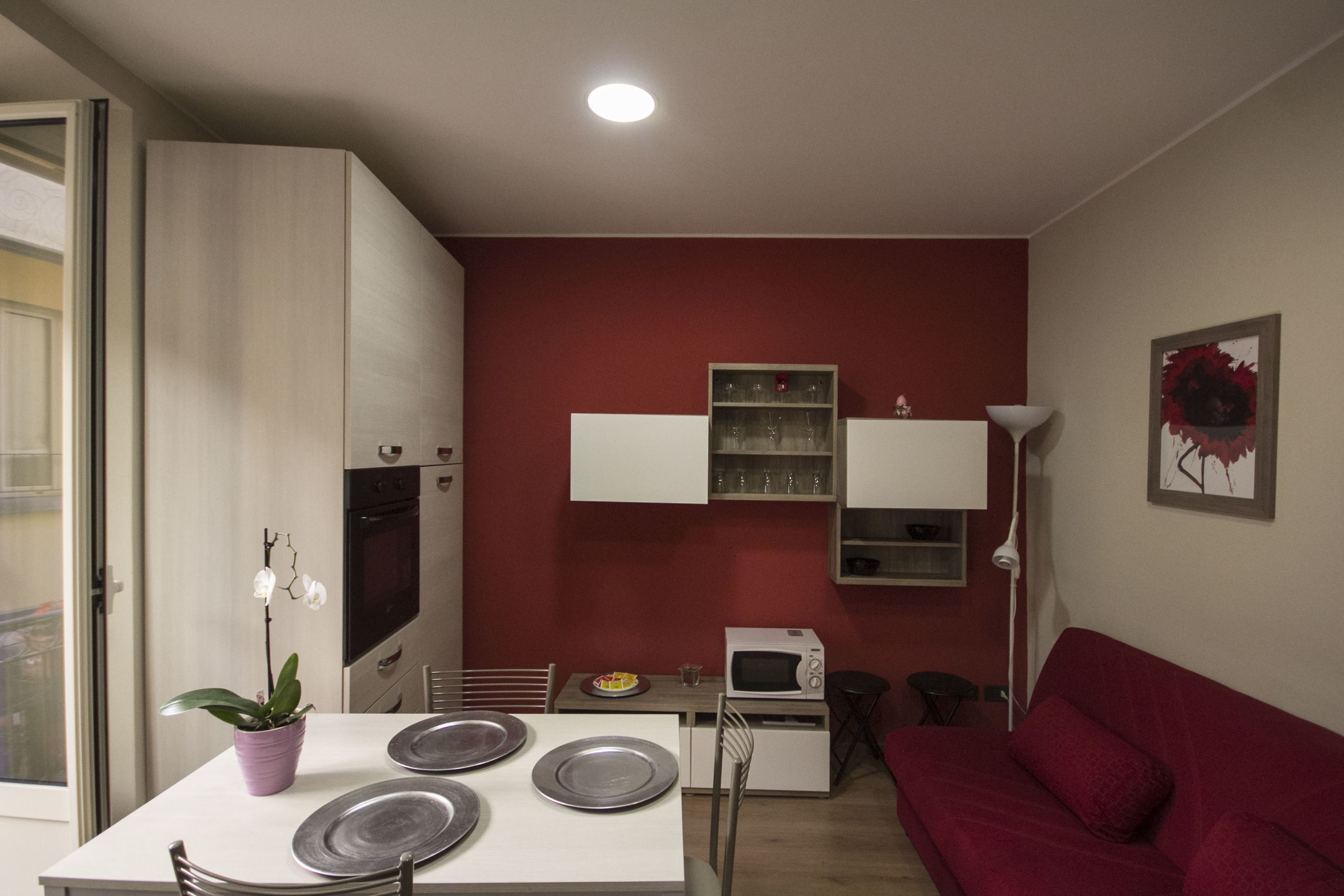 A compact living space with a kitchenette, a dining table with plates, a red sofa, and a potted plant.