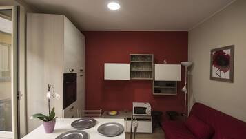 A compact living space with a kitchenette, a dining table with plates, a red sofa, and a potted plant.