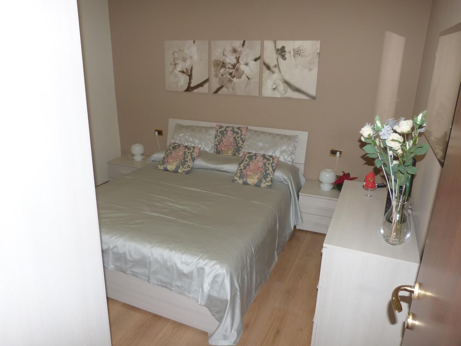 Un dormitorio con cama, mesitas de noche, cómoda y un florero con flores.