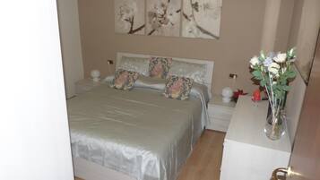 Un dormitorio con cama, mesitas de noche, cómoda y un florero con flores.