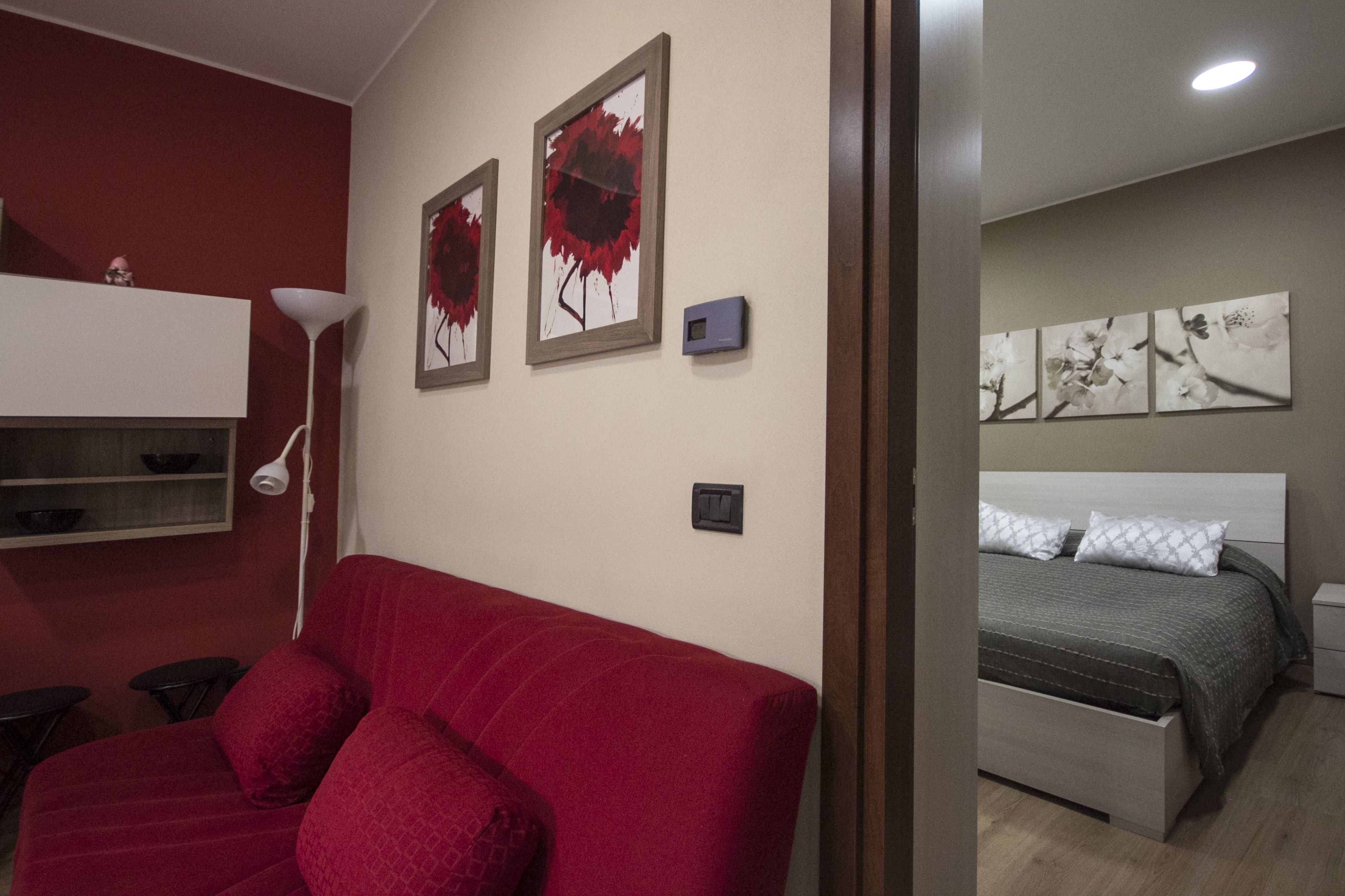 Een kamer met een rode bank, een bed met een grijs hoofdeinde en kunstwerken aan de muur.