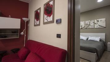 Een kamer met een rode bank, een bed met een grijs hoofdeinde en kunstwerken aan de muur.