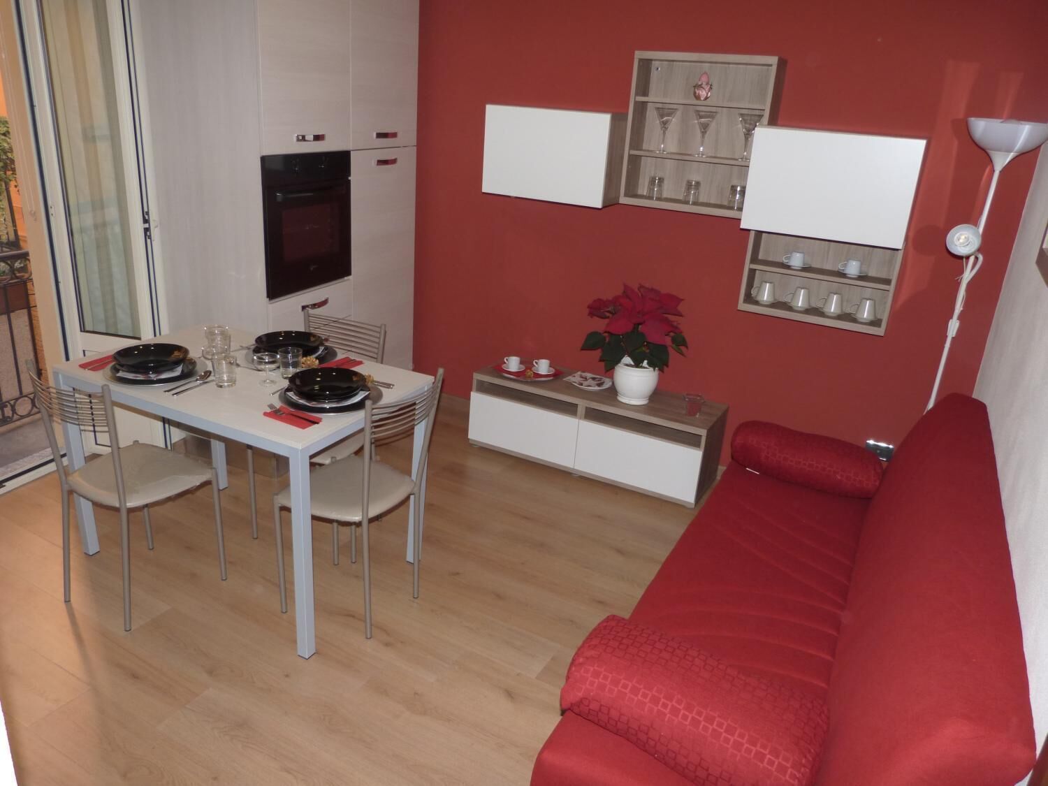 A compact living space with a dining area, a red sofa, a TV, and a small cabinet with glassware.