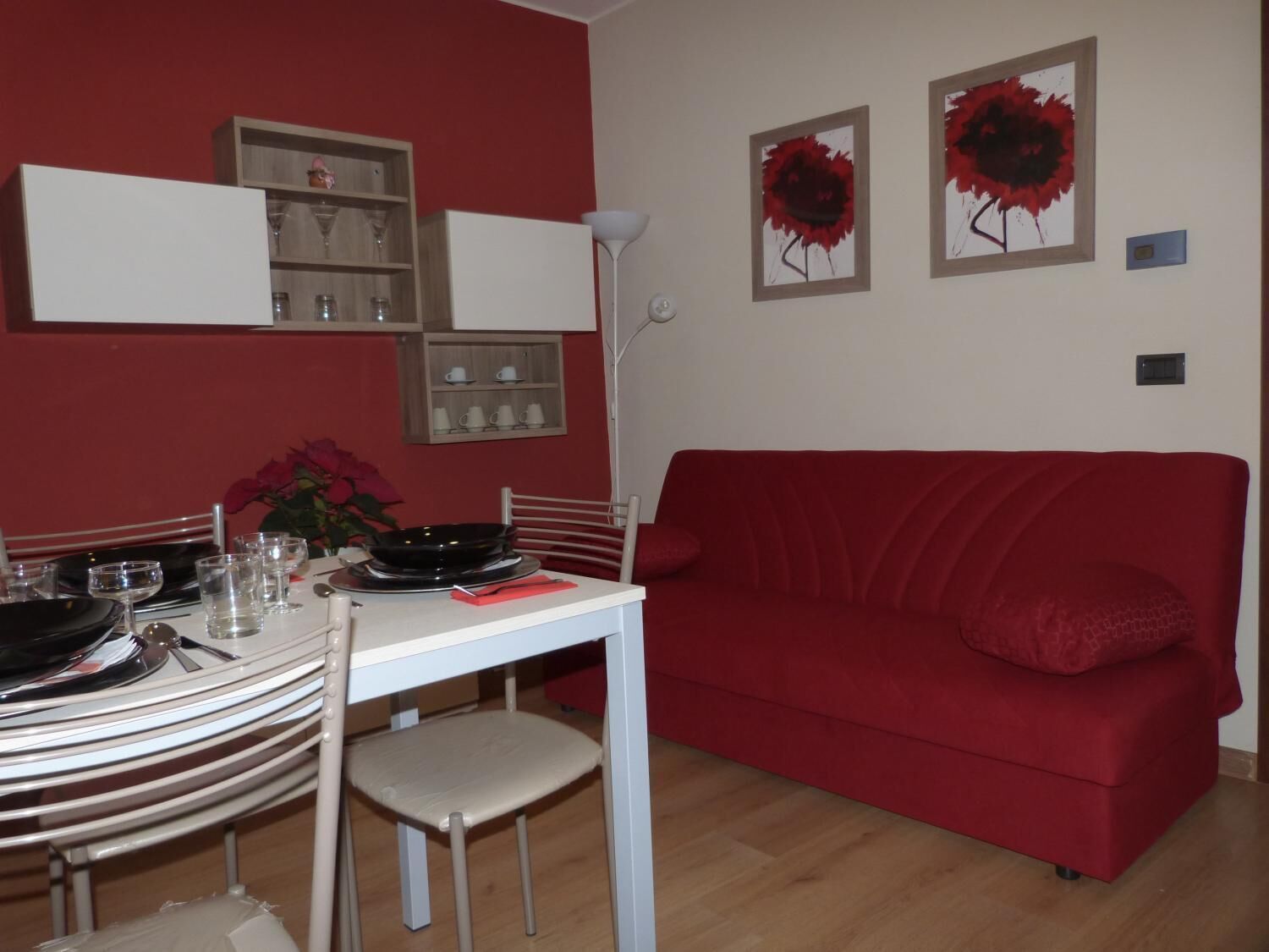 Un comedor con un sofá rojo, una mesa blanca y una silla. Hay dos obras de arte enmarcadas en la pared.