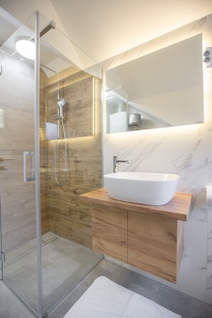 A modern bathroom with a glass-enclosed shower, a wooden vanity with a white sink, and a large mirror.