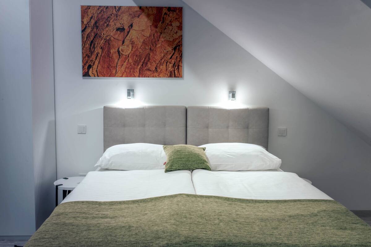 A modern bedroom with a large bed, two bedside lamps, and a large abstract painting on the wall.