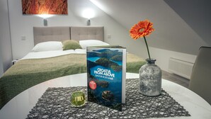 A neatly arranged bedroom with a bed, a book titled "Croatia from Above" by Davor Rostuhar, a vase with a flower, and a decorative glass on a table. - Apartments Beautiful You Are 2 (Zagreb)
