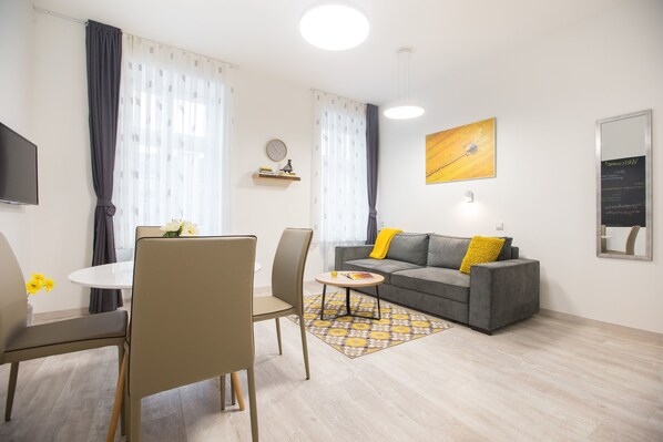 A modern living room with a grey sofa, a round coffee table, and a dining area with chairs.