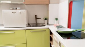 A kitchen with a white refrigerator, a stainless steel sink, and a stove with a green pan. - House Loft Foursquare (Thessaloniki)