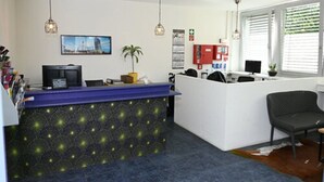 Zona de recepción con un mostrador azul, una computadora, una planta y una silla de oficina negra.