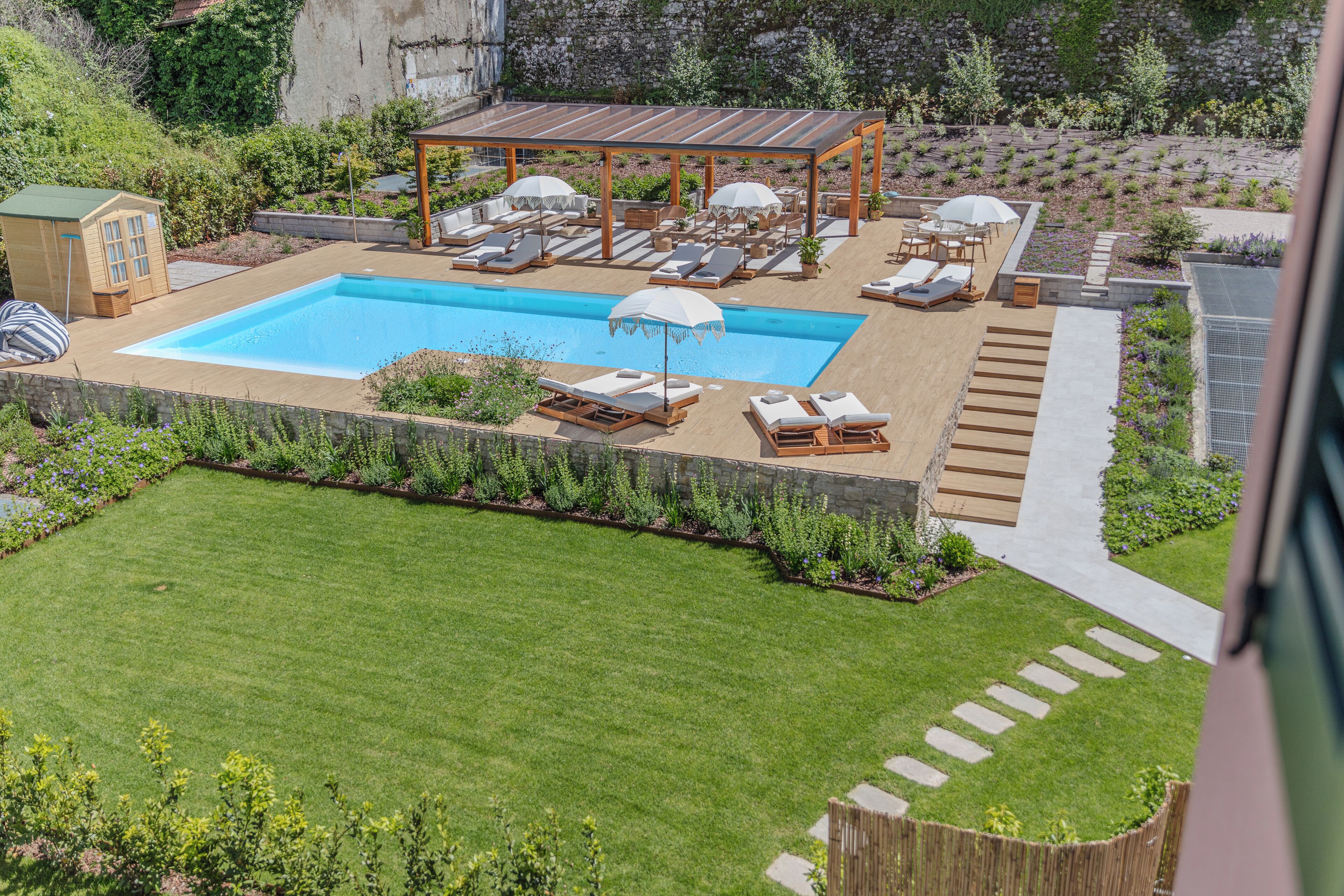 Patio con piscina, tumbonas, sombrillas y una terraza de madera.